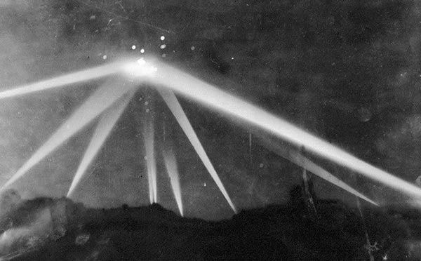 Long-exposure photo of the LA night-sky barrage: anti-aircraft tracers and searchlight cones over a city under wartime blackout.