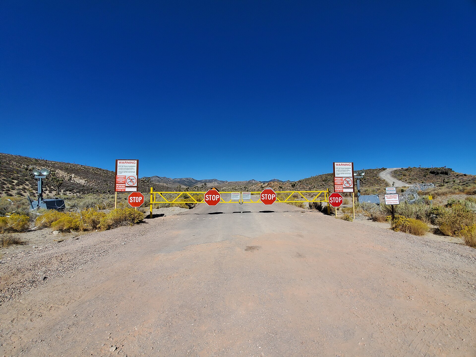 Area 51 main gate, photographed from the limit of public-access land. The 'use of deadly force authorized' signs and unmarked Cammo Dudes who track approaches are the closest most civilians ever get.